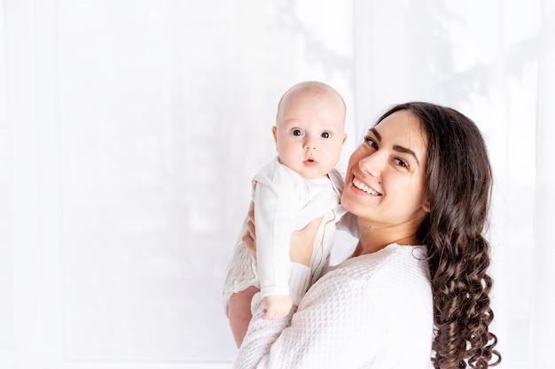 Madre feliz con hija en casa junto a la ventana, día de la madre, concepto de familia feliz, espacio para texto