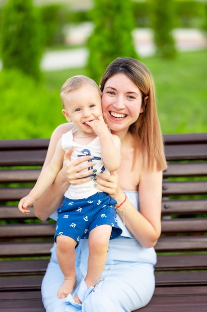 Una madre feliz con un hijo en el parque está sentada en un banco al aire libre y se divierte con un bebé en sus brazos