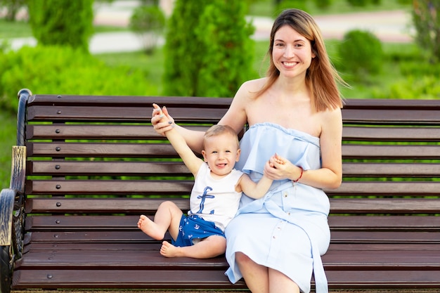 Una madre feliz con un hijo en el parque está sentada en un banco al aire libre y se divierte con un bebé en sus brazos