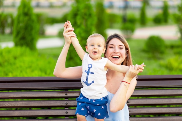 Una madre feliz con un hijo en el parque está sentada en un banco al aire libre y se divierte con un bebé en sus brazos