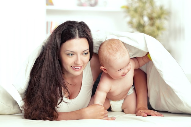 Madre feliz juega con el bebé acostado en la cama