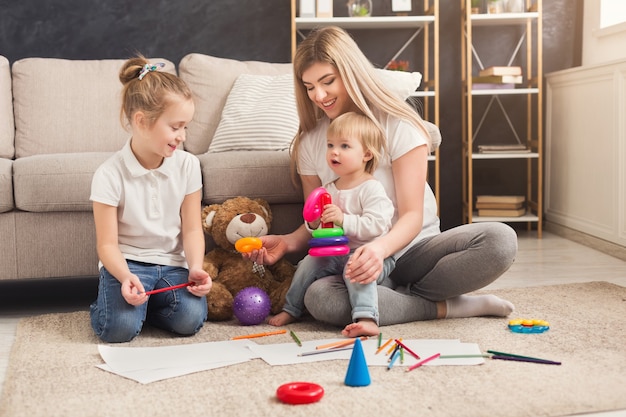 Madre feliz jugando y dibujando con sus dos hijos. Relación, maternidad, confianza, apoyo, caricia, calidez materna, cuidado, educación y concepto de desarrollo temprano.