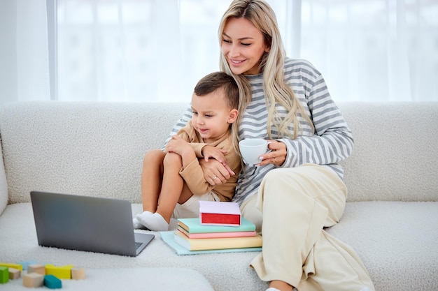 Madre feliz con lindo hijo encantador usando una computadora portátil viendo dibujos animados madre bonita y niño en edad preescolar sentado...