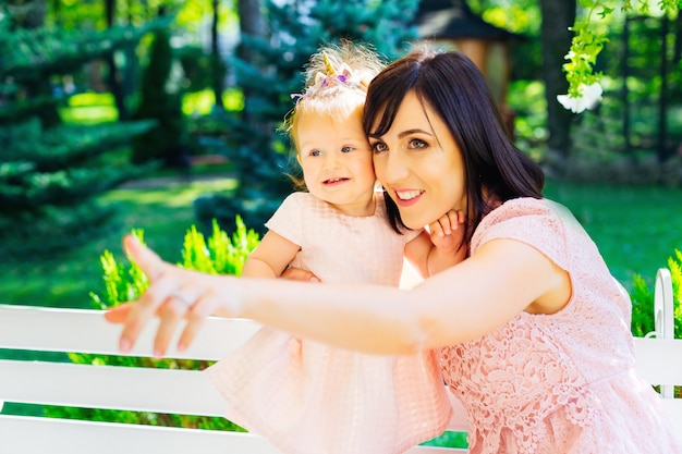 Madre feliz con un niño interesado en mirar la naturaleza en el parque y sentado en un banco blanco