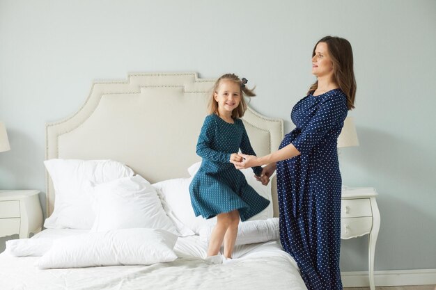 Madre feliz y pequeña hija saltando en la cama