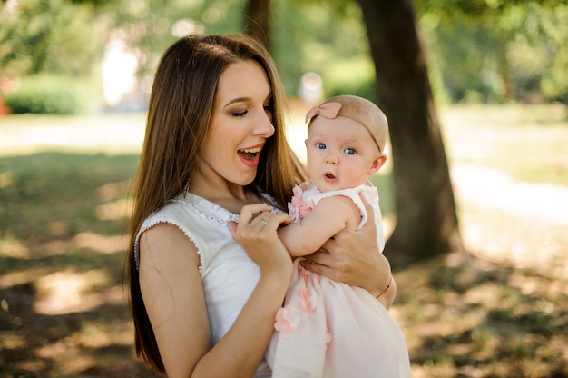 Madre feliz que detiene a su pequeña hija emocional en las manos en el parque