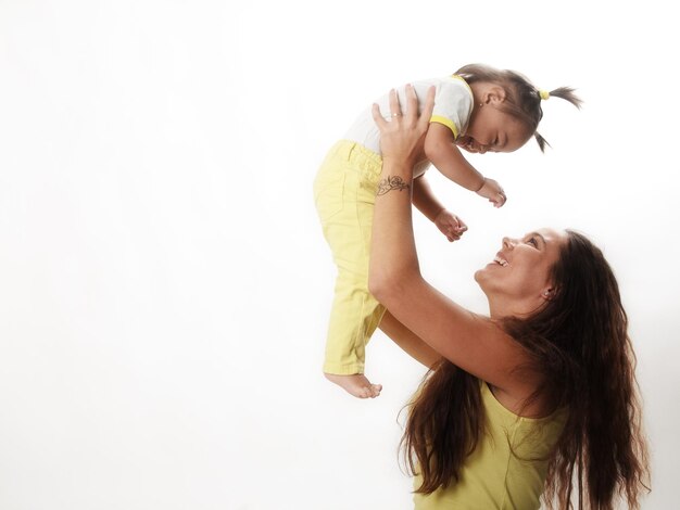 Foto madre feliz sosteniendo a su niña contra un fondo blanco