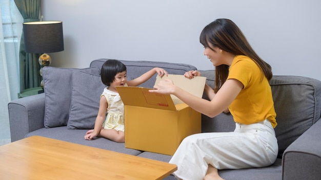 Una madre feliz con su hija abriendo una caja de cartón en el salón de casa