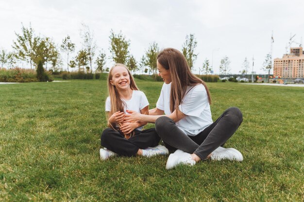 Una madre feliz y su hija están sentadas en el césped del parque y abrazando a la madre y la hija familia madre alegre y niña