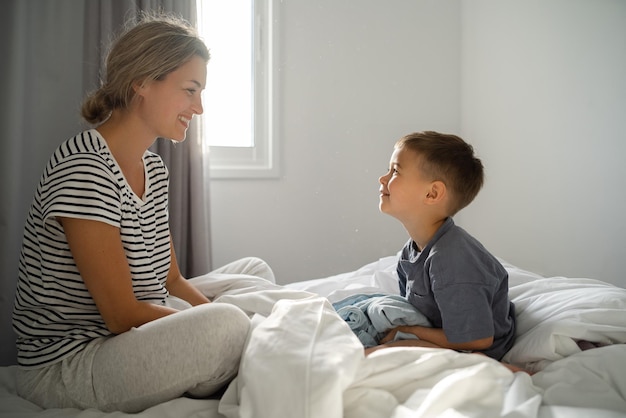 Una madre feliz y su hijo pequeño jugando alegremente en la comodidad de su cama