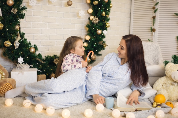 Madre feliz con su pequeña hija jugando cerca del árbol de Navidad