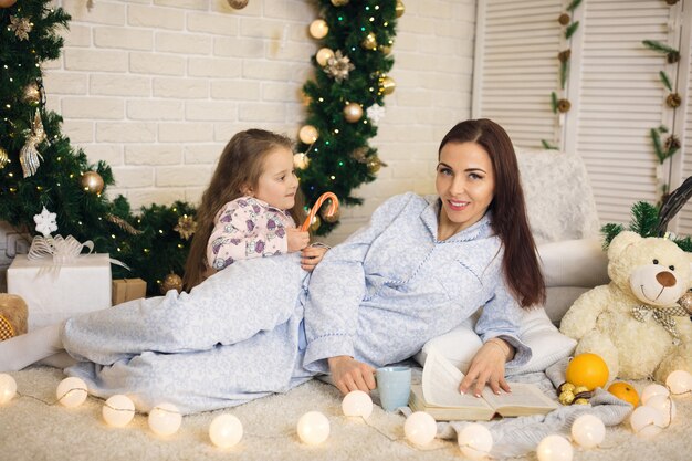 Madre feliz con su pequeña hija jugando cerca del árbol de Navidad