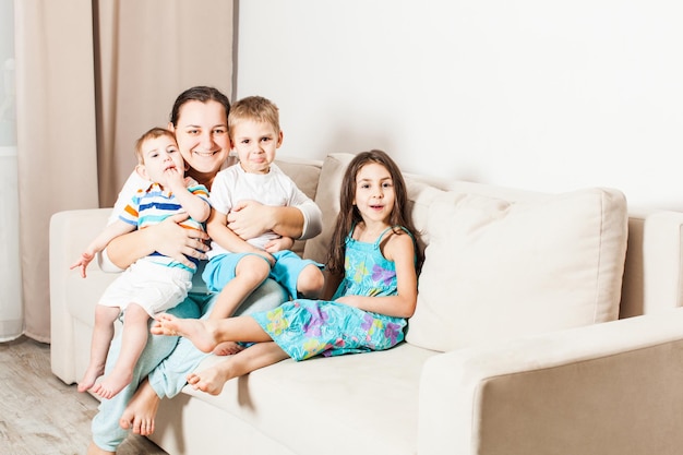 Madre feliz con sus tres hijos posando para una foto de familia. La niña sonríe y los niños están un poco aburridos.