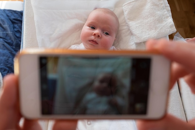 Foto la madre hace un retrato de su bebé en el teléfono móvil. recién nacido mirando a la cámara y sonriendo.