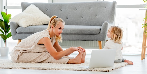 Madre haciendo ejercicio con su hijo en casa y viendo ejercicios de video en línea en la computadora portátil