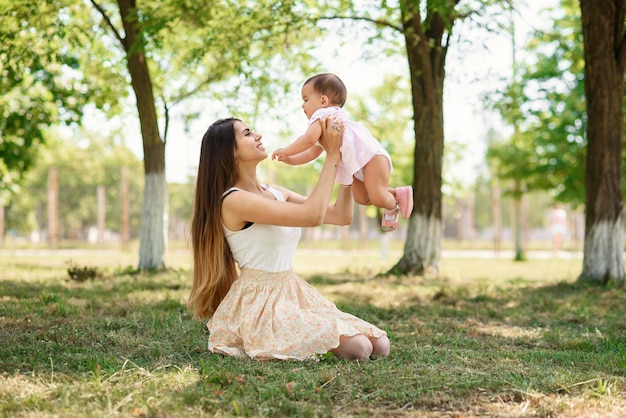 Madre hermosa joven que juega con un bebé en la hierba en un parque.