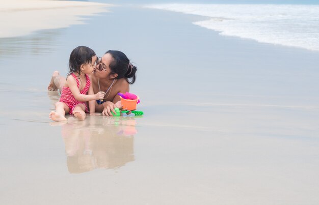 Foto la madre y la hija asiáticas están jugando y besándose juntas en la playa.