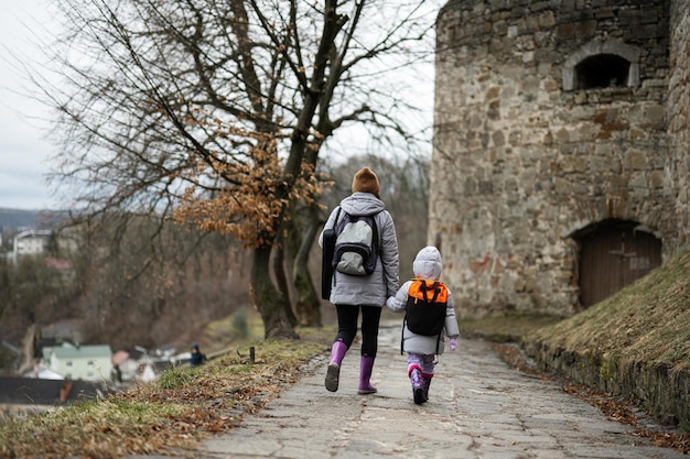 Madre con hija camina por un camino húmedo hacia una antigua fortaleza medieval bajo la lluvia Castillo de Terebovlia Ucrania