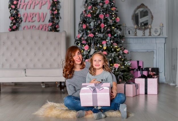 La madre y la hija cerca del árbol de Navidad sentados en el suelo