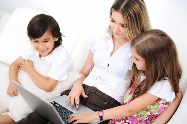 Madre con hija e hijo usando la computadora portátil en el sofá de interior