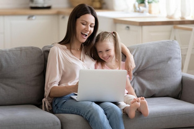 una madre y una hija están sentadas en un sofá y mirando una computadora portátil