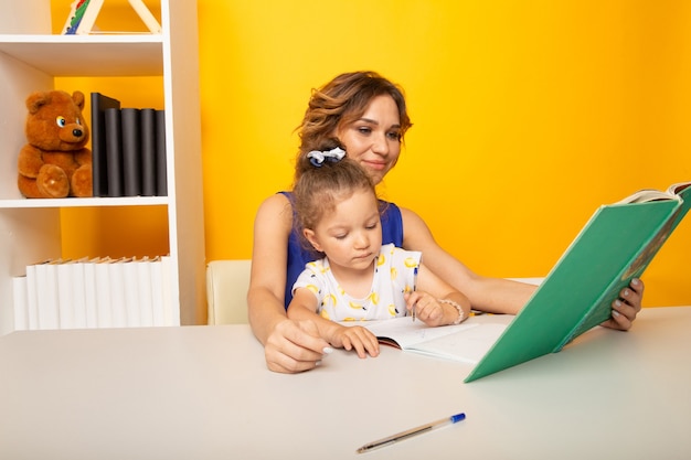 Madre con hija estudiando juntos sentados en casa