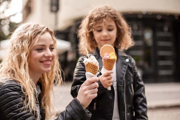 La madre y la hija felices sostienen un helado mientras caminan