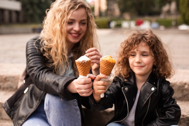 La madre y la hija felices sostienen un helado mientras caminan