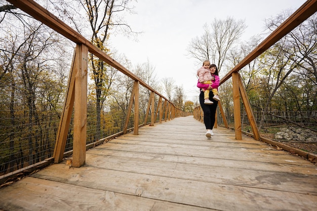 Madre con hija en manos caminando en el puente de madera