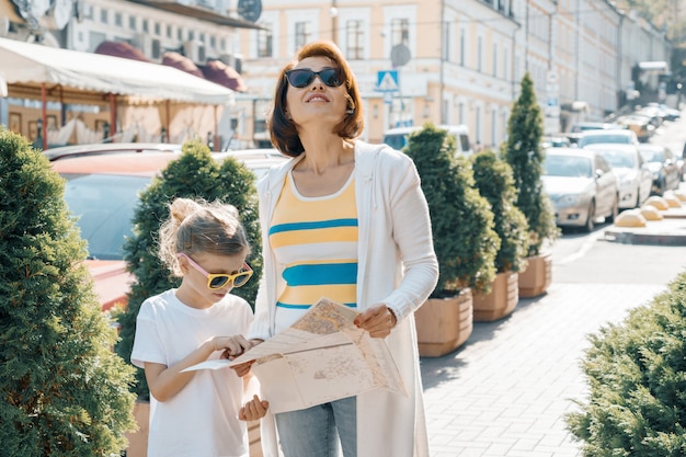 Madre con hija pequeña mirando el mapa de la ciudad y viajando juntos