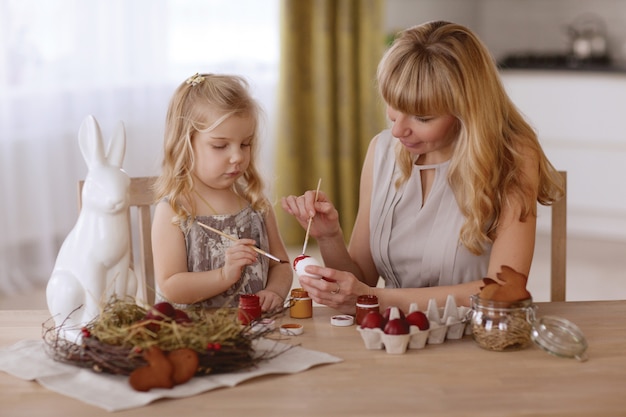 La madre y la hija pintan los huevos de Pascua en el cuarto en la tabla del día de fiesta.