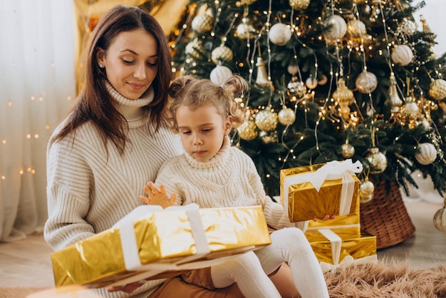 Madre con hija sosteniendo regalo de Navidad bajo el árbol de Navidad