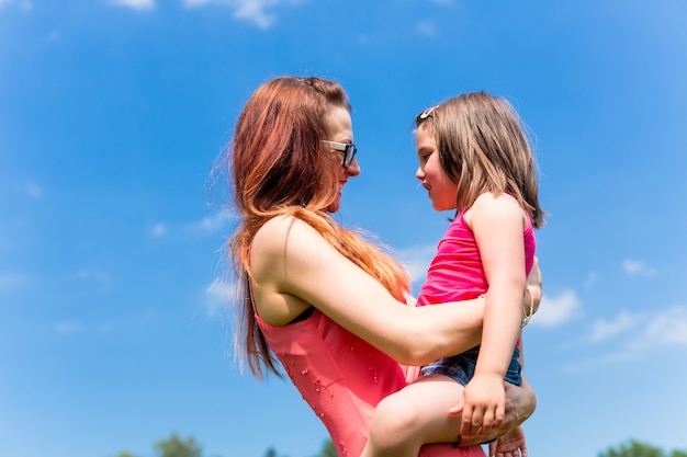 Madre con hija en su brazo bajo un cielo de verano azul claro