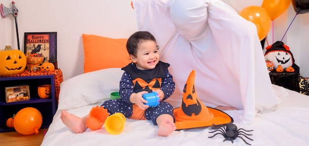 Madre con hija en traje para celebrar Halloween en casa. Niño con mamá en la decoración del dormitorio en temporada de otoño.