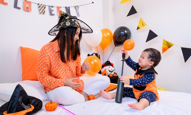 Madre con hija en traje para celebrar Halloween en casa. Niño con mamá en la decoración del dormitorio para truco o trato en la temporada de otoño.