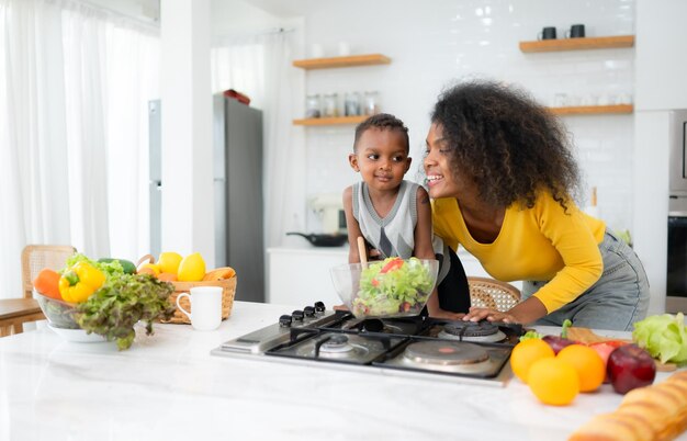 Madre y hijo afroamericanos preparando ensalada juntos en la cocina de casa