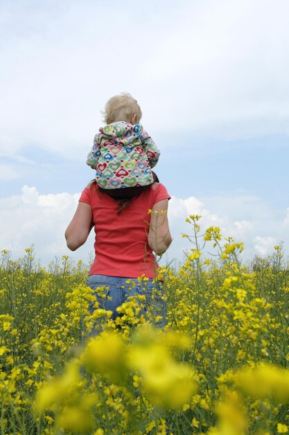 Madre con hijo en un campo amarillo en flor con cielo azul y nubes blancas