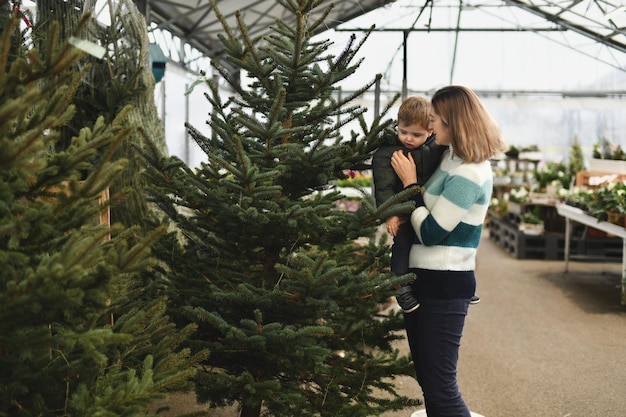 La madre y el hijo compran un árbol normando de Navidad en una tienda