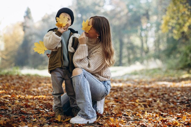 Madre con hijo divirtiéndose en el parque otoñal jugando con hojas