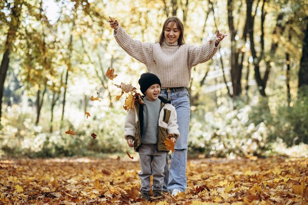 Madre con hijo divirtiéndose en el parque otoñal jugando con hojas