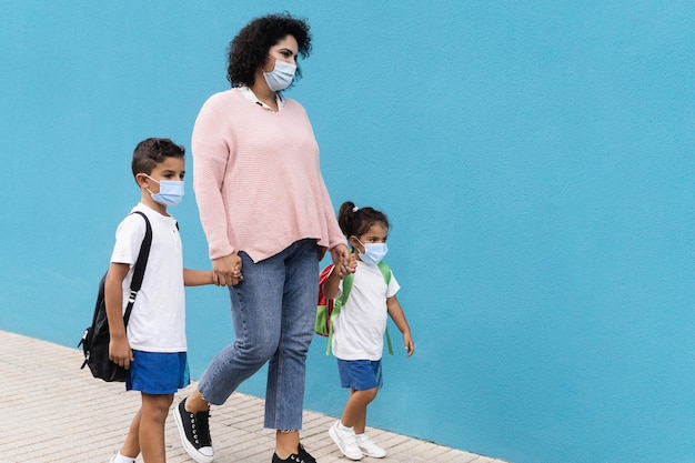 Madre con hijo e hija que regresan a la escuela con máscaras de seguridad - Concéntrese en la cara de mamá