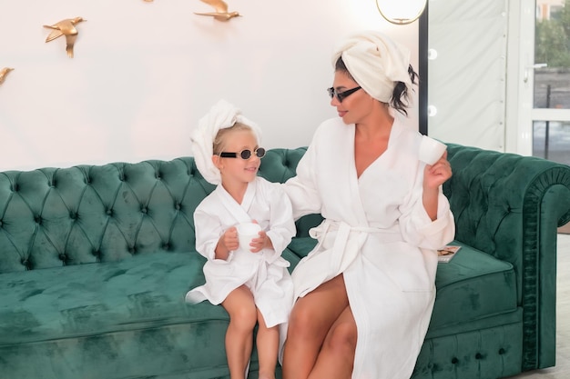 Madre con hijo haciendo tratamiento de belleza juntos Familia feliz madre y hija hija en toalla y bata están sentadas en el sofá concepto de salón de belleza spa de bienestar formato de pancarta larga