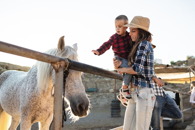 Madre con hijo pequeño divirtiéndose a caballo en el rancho de la granja - Centrarse en la cara de mamá