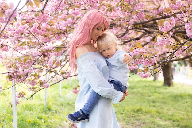 Madre con hijo pequeño en el paseo del parque cerca del árbol de sakura