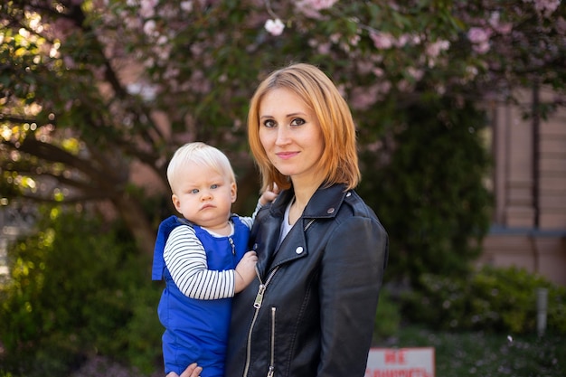 Madre con hijo pequeño en el paseo del parque cerca del árbol de sakura