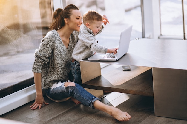 Madre con hijo pequeño que trabaja en la computadora en casa