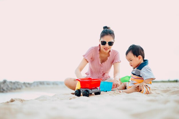 Madre y hijo sonrientes sentados en la playa contra el cielo