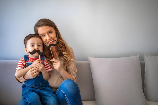 Madre con hijo sosteniendo bigote de fotomatón Mujer y niño sobre un fondo gris