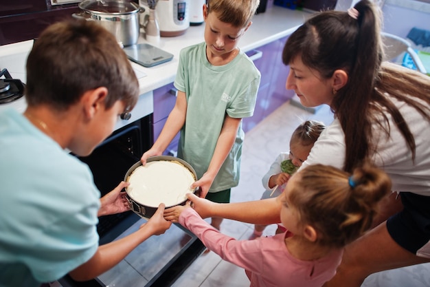 Madre con hijos cocinando en la cocina momentos infantiles felices Tarta de queso en el horno