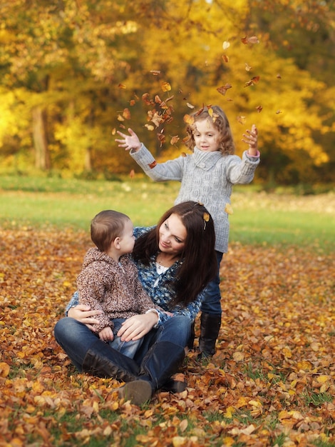 Foto madre con hijos sentados en hojas en el parque durante el otoño